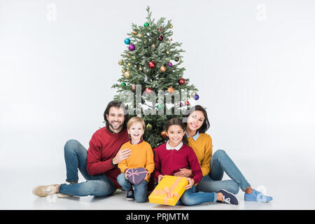 La famiglia felice seduta vicino ad albero di natale con presenta isolato su bianco Foto Stock