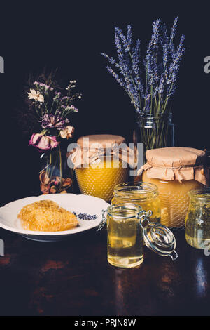 Messa a fuoco selettiva dei vasi con miele, fiori secchi, lavanda e un nido su sfondo nero Foto Stock