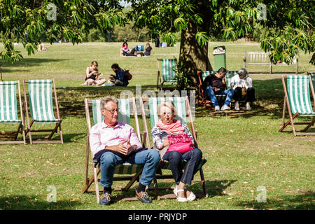 Londra Inghilterra,Regno Unito,Parchi reali,Hyde Park,parco,spazio verde,prato,albero,sedie a sdraio,uomo uomini maschio,donna donne,coppia,maturo,crogiolarsi al sole,prendere il sole Foto Stock