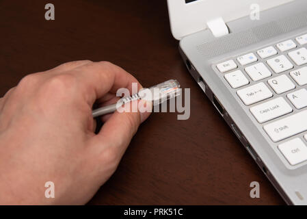 Primo piano lato cavo di collegamento per la connessione di rete a una porta LAN di un computer portatile sul tavolo di legno, concetto di collegamento del computer. Foto Stock
