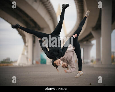 Eseguire le ragazze si divide in aria durante il salto sul background urbano del ponte Foto Stock