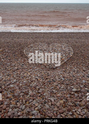 Grande amore forma di cuore realizzata con ciottoli sulla spiaggia. Raccolto verticale. Foto Stock