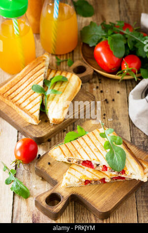Concetto di prima colazione. Frutta e succhi freschi e deliziosi panini fatti in casa con tonno, pomodoro, formaggio su una cucina in legno tavolo. Foto Stock