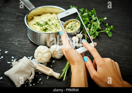 La donna ha le mani tenendo il telefono cellulare e scattare una foto di una deliziosa purea di patate su una tavola di legno Foto Stock