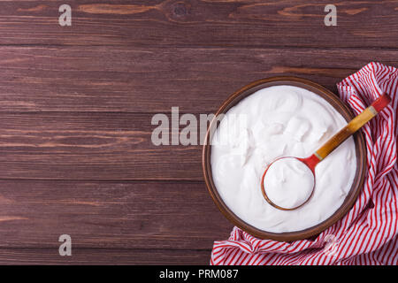 Yogurt nella piastra di argilla con cucchiaio su sfondo di legno Foto Stock