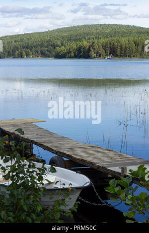 Lago di foresta con cottage. Barca legato al molo in primo piano. Foto Stock