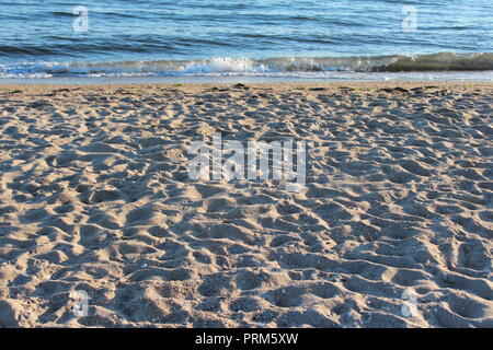 Spiaggia con molte tracce da un giorno felice dalla battigia. Ancora onde che lambiscono dolcemente sulla riva. Foto Stock