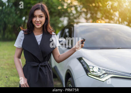 Giovane donna tenendo premuto il tasto smart remote con un auto Foto Stock