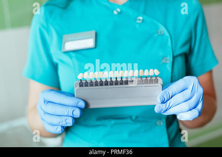 Dentista tenendo in corrispondenza delle mani la tonalità o il colore degli impianti o il processo di sbiancamento dei denti. Foto Stock