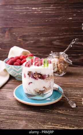 Layered yogurt con granola e lamponi. In un bicchiere e decorate con foglie di menta. On dark tavola in legno rustico sfondo. Cibo sano concetto. Foto Stock