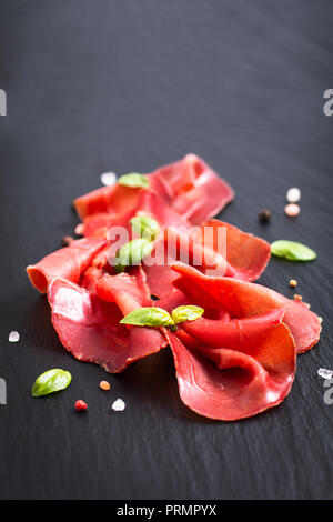 Alimentare il concetto di antipasti affettato essiccate indurite potenzia la Bresaola su nero ardesia scheda di pietra Foto Stock