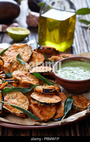 Impanata Melanzane fritte fette di melanzane su una piastra di terracotta con yogurt prezzemolo immersione nel recipiente di argilla su un tavolo rustico con ingredienti sul retro Foto Stock