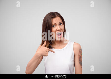 Si intende per me? Una foto di un perplesso confuso giovane bella donna vestita di un top bianco guardando la telecamera con la sua mascella caduta, rivolta a lei Foto Stock