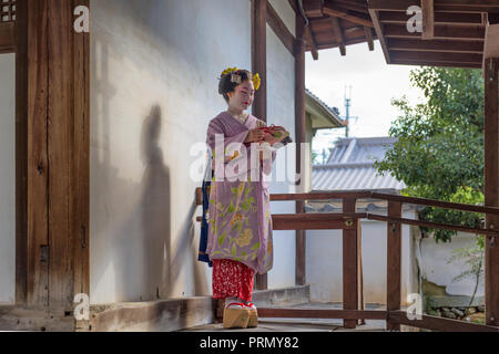 KYOTO, Giappone - 28 novembre 2015: una donna nel tradizionale abito Maiko si affaccia da un tempio porta. Foto Stock