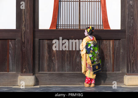 KYOTO, Giappone - 28 novembre 2015: una donna nel tradizionale abito Maiko si affaccia da un tempio porta. Foto Stock