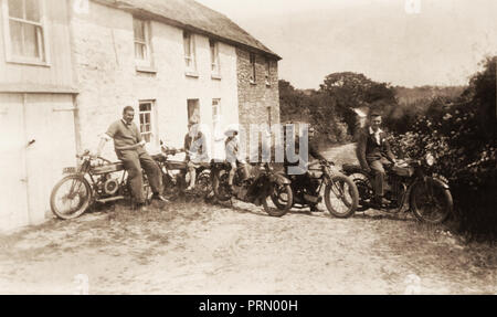 Un gruppo di tre uomini e una donna e giovane ragazzo seduto sul veterano 1920's motocicli, compreso un Royal Enfield 350cc, al di fuori di cottages in Cornovaglia circa 1 Foto Stock