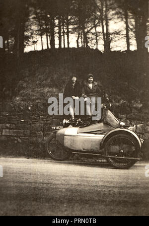 Due signore prendendo una pausa dai loro viaggi seduti sulla sommità di un muro di pietra dietro di loro veterano moto & sidecar combinazione a lato della strada circ Foto Stock