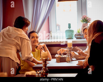 Un gruppo di donne adulte si trova in un accogliente bar. Le ragazze si guardano reciprocamente e parlare. Foto Stock