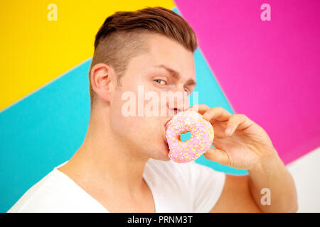 Bella bionda uomo su sfondo colorato di mangiare una ciambella di rosa Foto Stock