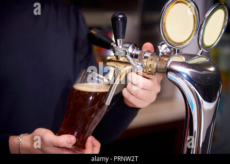 Il barman si versa la birra dal rubinetto in vetro. Foto Stock