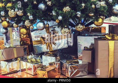 Pacchetti di natale con doni nelle mani della ragazza accanto all'albero di Natale e un sacco di scatole con il nuovo anno di regali di Natale. Foto Stock