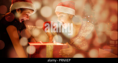 Immagine composita di festosa madre e figlia apertura di un incandescente regalo di natale Foto Stock