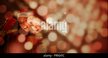 Immagine composita di festosa madre e figlia apertura di un regalo di natale Foto Stock