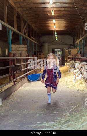 Sorridente kid in esecuzione nel fienile con capre al maso Foto Stock