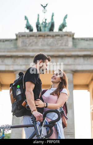 Basso angolo di vista sorridente viaggiatori femmina abbracciando il fidanzato davanti la porta di Brandeburgo, Berlino, Germania Foto Stock