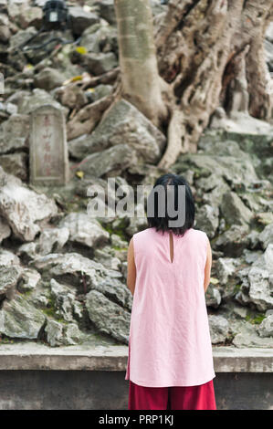 Donna orante presso un santuario tradizionale ad Hanoi, Vietnam. Decorazione di lastre di pietra su un antico hillside. Foto Stock