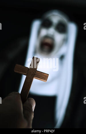 Primo piano con una croce in mano di un uomo e di una spaventosa male nun, indossando un tipico bianco e nero abitudine, urlando Foto Stock