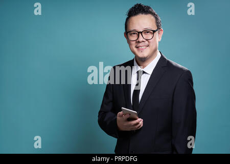 Ritratto di sorriso imprenditore asiatici in tuta con utilizza lo smartphone . isolato su fondo azzurro . Foto Stock