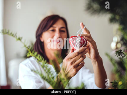 Un senior donna decorare un albero di Natale a casa. Foto Stock