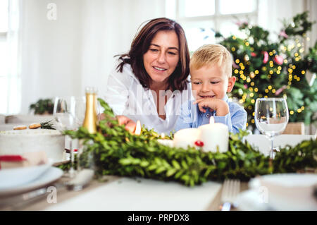 Un piccolo ragazzo con la nonna seduta al tavolo a casa al tempo di Natale. Foto Stock
