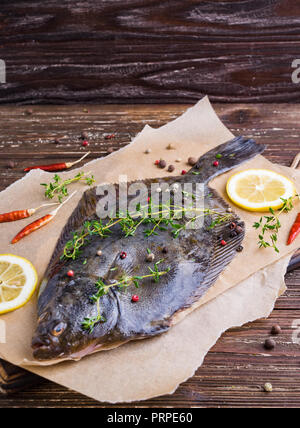 Materie passera di mare Passera di mare pesce (pesci piatti). Il processo di cottura del concetto. La Passera pianuzza Pesce con spezie, le fette di limone, timo su carta pergamena. Legno scuro tabella bac Foto Stock