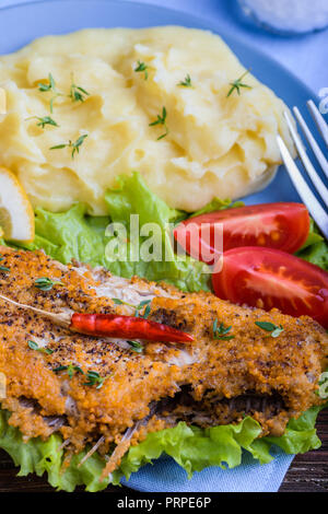 Frittura di pesce piatto su insalata verde con purè di patate, pomodori, pepe e le fette di limone in blu sulla piastra scuri in legno rustico sfondo. La deliziosa cena Foto Stock