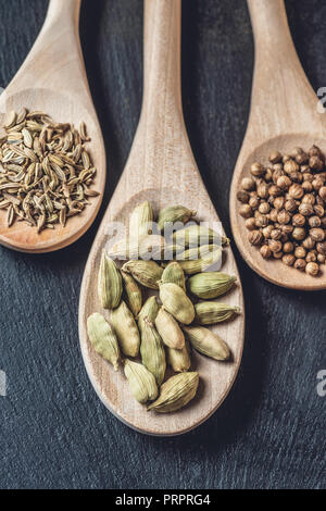 Vista ravvicinata di cucchiai di legno con il cardamomo e i semi di coriandolo e di cumino su nero Foto Stock