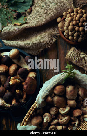 Vista superiore assortiti di materie i funghi commestibili in basket e bocce, il sacco e la fune sul tavolo di legno Foto Stock