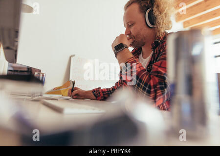 L'uomo facendo alcune note in copybook, seduti al piccolo ufficio tavolo. Esperienza professionale tech codifica su un blocco note in ufficio. Foto Stock