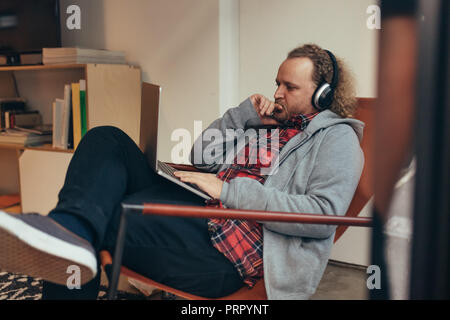 Uomo in casuals rilassarvi su una poltrona guardando al suo laptop e pensare. Programmatore di computer a lavorare su un nuovo software di sviluppo. Foto Stock
