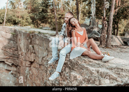 Bella dai capelli scuri donna appoggiata al suo uomo forte mentre è seduto vicino a scogliere Foto Stock