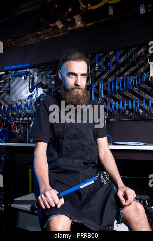 Ritratto di proprietario di piccola impresa del giovane uomo con la barba. Guy bicicletta officina meccanica lavoratore seduto con lo strumento in mano a un gruppo di lavoro di vestire nero Foto Stock