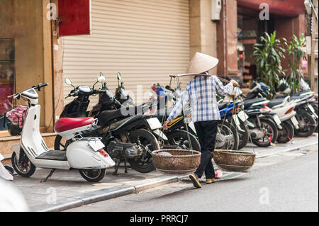 Donna che indossa un tessuto tradizionale riso hat sulle strade di Hanoi, Vietnam. Foto Stock