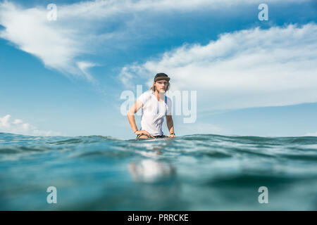 Surfista maschile seduto sul bordo di surf in oceano presso la spiaggia di Nusa Dua, Bali, Indonesia Foto Stock