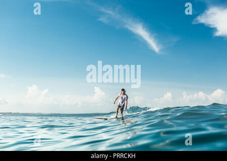 Vista in lontananza surfista maschio equitazione sulla scheda di navigazione in oceano presso la spiaggia di Nusa Dua, Bali, Indonesia Foto Stock