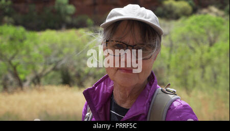 Una sana attiva donna backpacking all'aperto sorridente in telecamera con vento che soffia Foto Stock