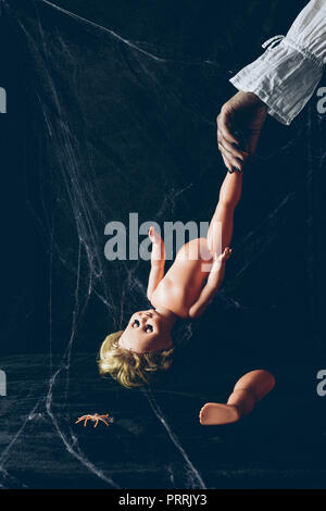 Vista parziale di scary donna holding creepy doll nel buio con spider web Foto Stock