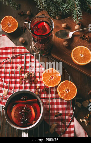 In casa vin brulé in coppa di vetro e la pentola sul tavolo di legno con spezie e arance fresche Foto Stock