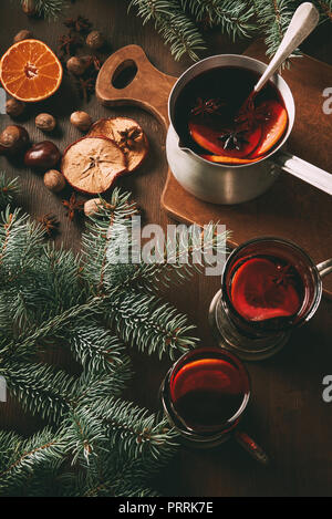 Vin brulé in casseruola e tazze di vetro con spezie su sfondo di legno con rami di abete Foto Stock