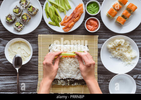 Ritagliato colpo di persona la cottura delizioso sushi roll con salmone, avocado e cetrioli Foto Stock